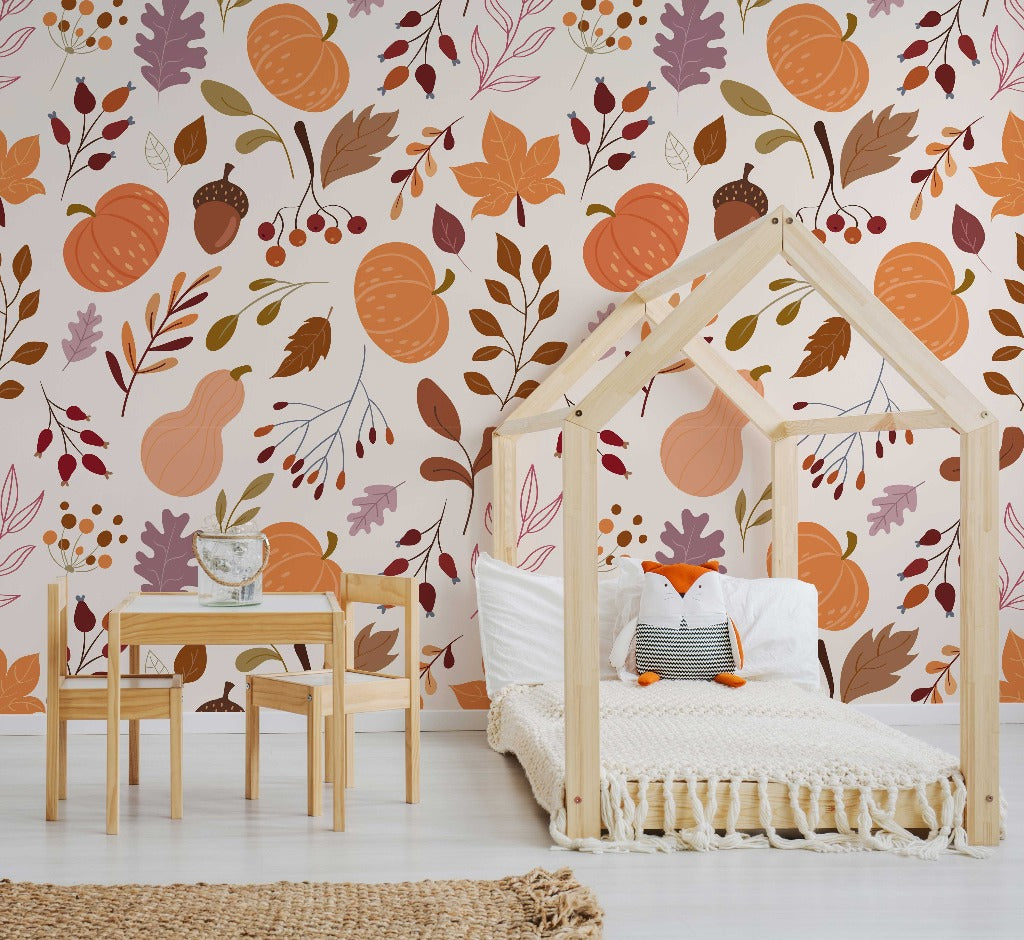 A cozy children's bedroom with a house-shaped wooden bed frame, decorated with Decor2Go Wallpaper Mural featuring a Pumpkins & Leaves illustration, a small wooden table and chairs, and a woven rug on the floor.