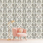 A modern room with a light pink armchair and gold floor lamp in front of an intricate Decor2Go Wallpaper Mural in shades of green and gray featuring the Vintage Owls Garden design.