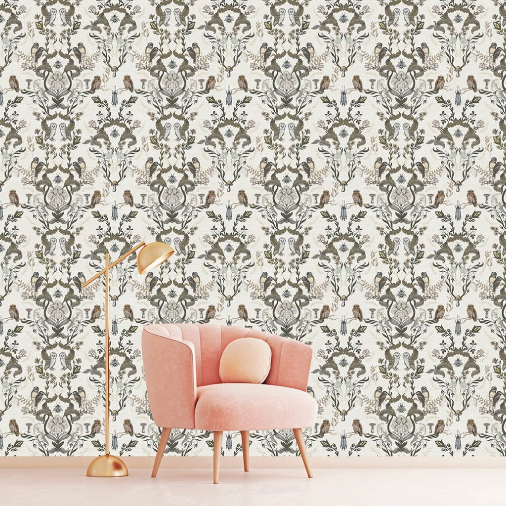 A modern room with a light pink armchair and gold floor lamp in front of an intricate Decor2Go Wallpaper Mural in shades of green and gray featuring the Vintage Owls Garden design.