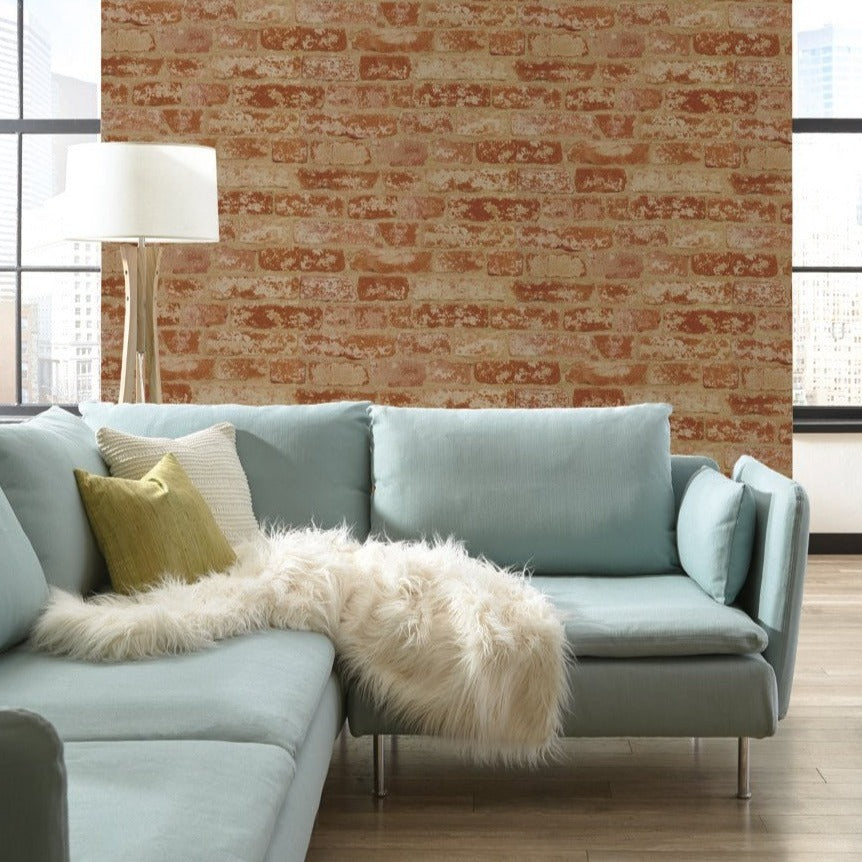 A modern living room features a light blue sectional sofa with a furry white throw and green, white, and yellow pillows. A tall white floor lamp stands behind the sofa. The room has large windows and York Wallcoverings Urban Chic Up The Wall Wallpaper (56 SqFt) as an accent wall, creating a bright and cozy atmosphere.