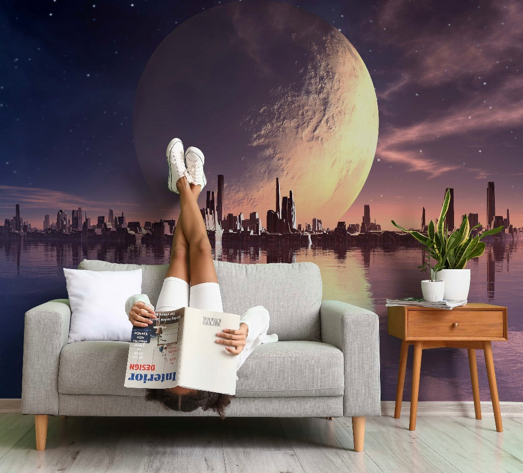 A person lounges on a gray sofa, reading a book with legs up, white sneakers on, against the surreal backdrop of a Decor2Go Wallpaper Mural depicting a city skyline and an oversized moon.