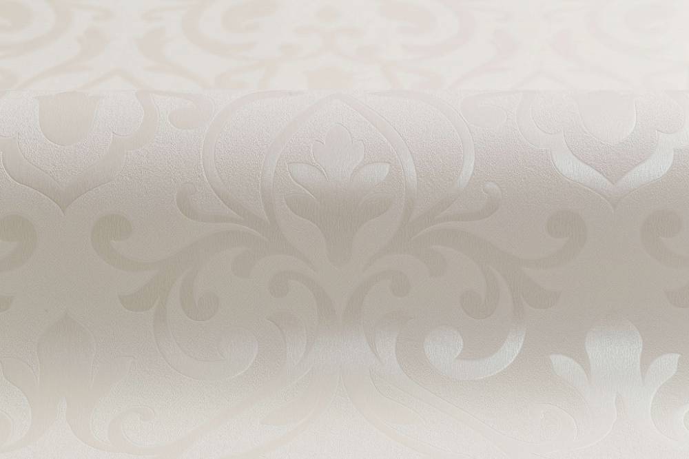 A close-up view of an elegant, textured wallpaper featuring a subtle, intricate damask pattern in a light cream color. Enhanced with modern hot stamping techniques, the design showcases symmetrical, decorative floral and scroll motifs, giving the Rhodonis Wallpaper (114 SqFt) by Palitra a luxurious and sophisticated appearance.