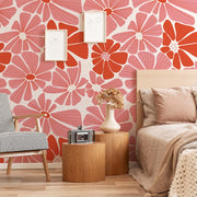 Bedroom - A cozy bedroom corner featuring a bed with pink linens, a Decor2Go Wallpaper Mural with a groovy daisy flower pattern, a wooden side table with a vintage camera, and a chair with checkered upholstery.