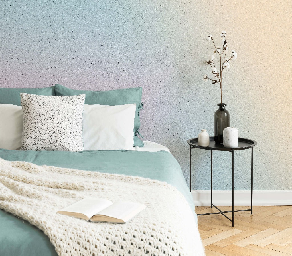 A cozy bedroom corner featuring a bed with teal and white bedding, a round black side table with a vase and candles, and an open book on the bed, against Decor2Go Wallpaper Mural.