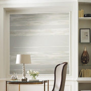 Home Office - A modern with a sleek white desk adorned with a white lamp, small vase of flowers, and stationery. Behind the desk is a large artwork featuring York Wallcoverings Horizontal Dry Brush Wallpaper (60 SqFt) in neutral tones. To the right, there are built-in shelves holding books, decor, and framed art