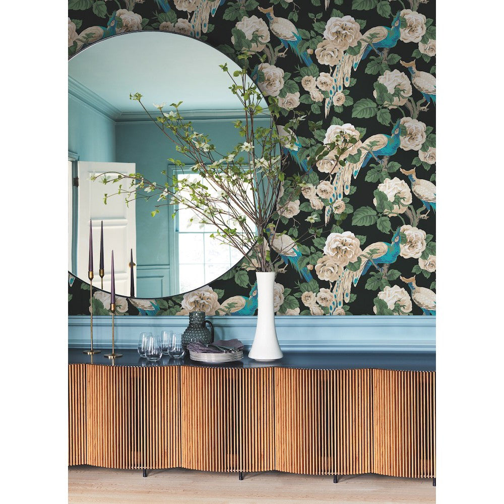 Entryway - A chic features a circular mirror above a black console table decorated with a vase of branches, a white pitcher, several candles, and glassware. The wall behind is adorned with York Wallcoverings' Garden Plume Wallpaper (60 SqFt) featuring bold floral designs and colorful plumage in shades of green, blue, and white