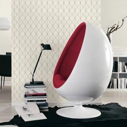 A modern, egg-shaped white chair with a red cushioned interior sits on a black rug in front of a bookcase and wall adorned with Ontario Diamond Geometric Wallpaper (56 SqFt). A black desk lamp is placed on a stack of books next to the chair in the contemporary room.