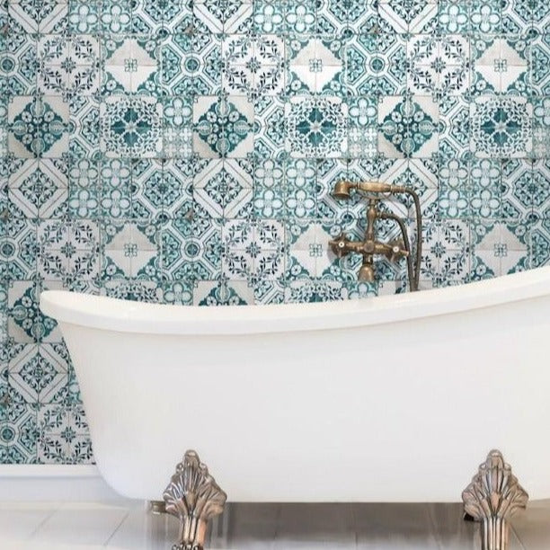 Bathroom - A white clawfoot bathtub stands against a wall adorned with intricate blue and white patterned tiles. The vintage-style brass faucet complements the bathtub's classic feet, enhanced by the use of York Wallcoverings' Mediterranean Tile Wallpaper, creating a luxurious and timeless setting