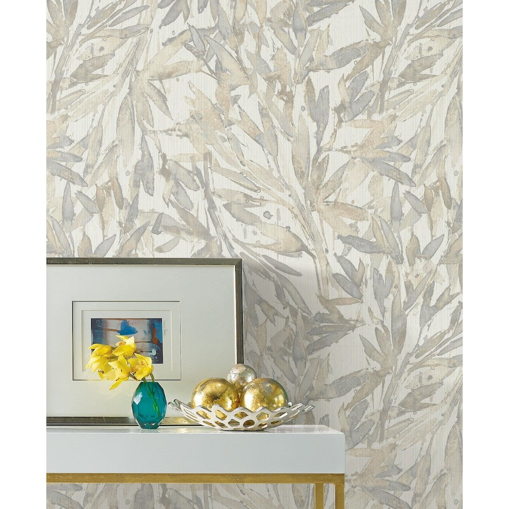 A white table with a silver frame photo, a teal vase with yellow flowers, and a decorative bowl with silver and gold ornaments. The background features Rainforest Leaves (56 SqFt) Wallpaper by York Wallcoverings in shades of beige and gray.